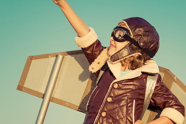 young child wearing a pilot outfit and wings